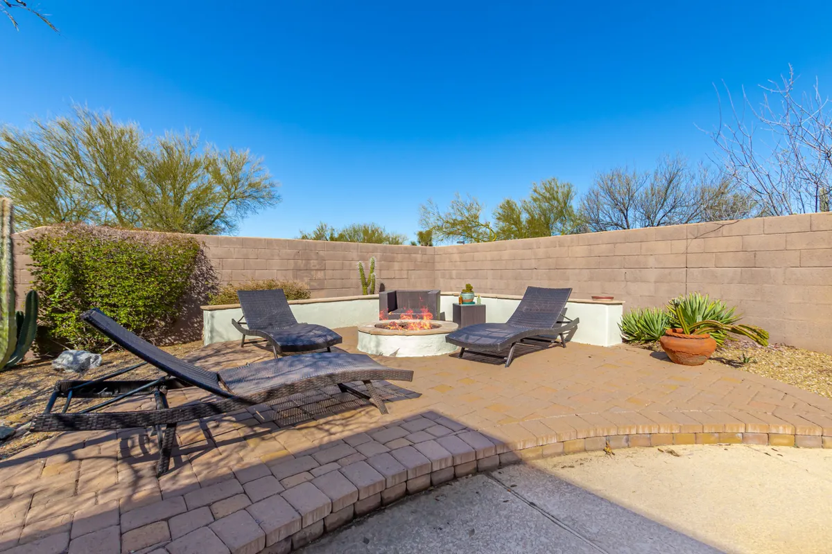 This image centers on a modern fire pit surrounded by comfortable lounge chairs and lush greenery, creating the perfect spot for evening relaxation. The scene suggests cozy gatherings, stargazing, and intimate conversations under the desert sky.
