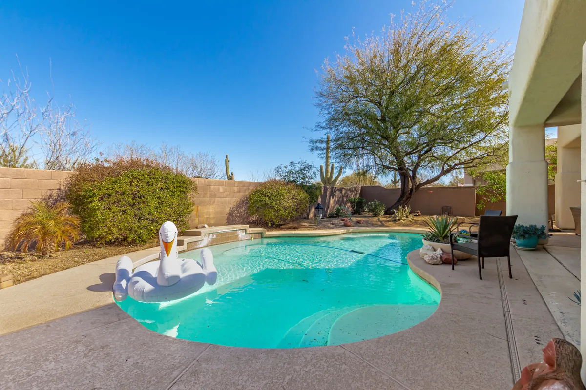 A stylish backyard oasis with a sparkling swimming pool, an inflatable swan float, and manicured landscaping. The setting is perfect for relaxing or socializing after a day on the golf course.