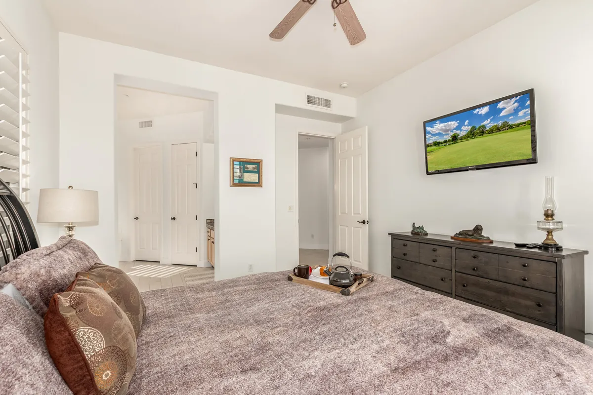 A tranquil bedroom featuring a bed with a textured bedspread, a TV mounted on the wall, a nightstand with a lamp, and decorative items that create a soothing atmosphere.