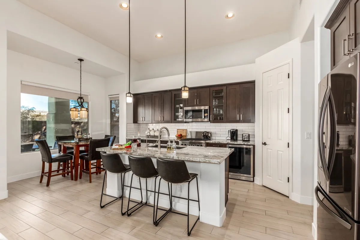 This image features a kitchen with a central island topped with a granite countertop, surrounded by bar stools. Stainless steel appliances and a window offering natural light complete the scene, giving a warm, welcoming atmosphere ideal for meal preparation and casual gatherings.