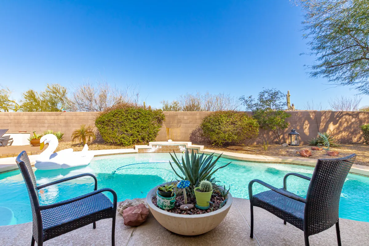A tranquil outdoor area with a sparkling swimming pool, potted plants, outdoor chairs, and a decorative swan float. The scene is peaceful and inviting, ideal for relaxing or spending quality time together.