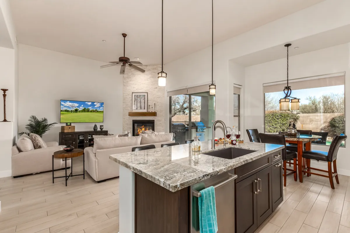 An open-concept space blending the kitchen, living area with a sofa, television, and dining table. Natural light pours in through large windows, highlighting the seamless flow between areas and the inviting, relaxed atmosphere.